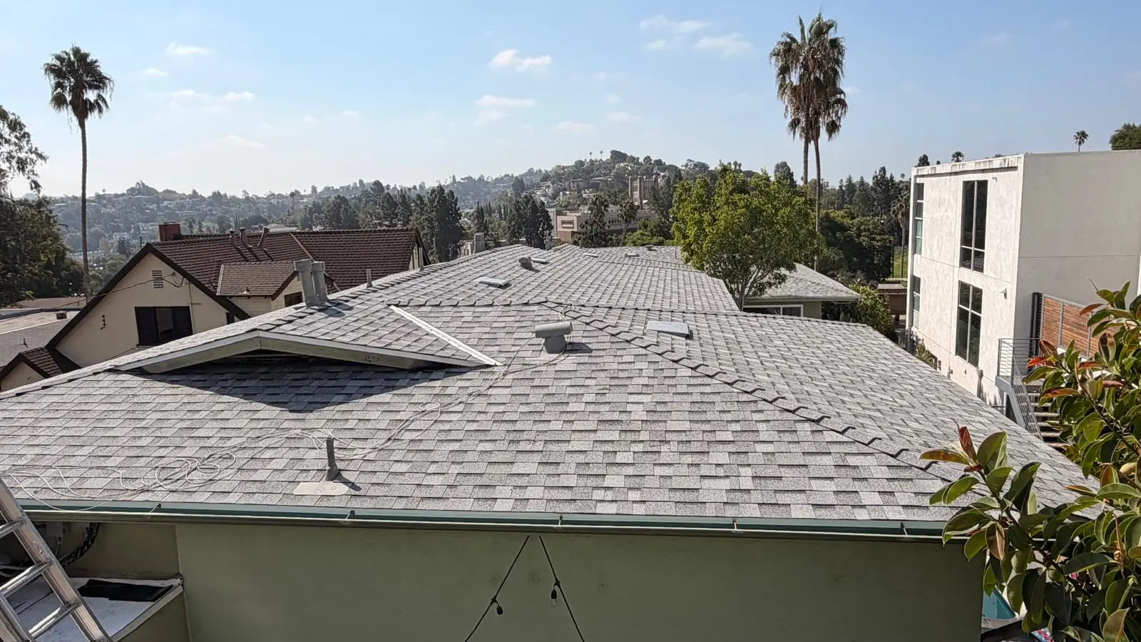 Finished gray shingle roof on a two-story Los Angeles apartment building with hillside homes behind it