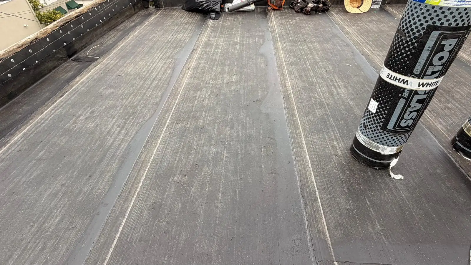 A roll of white Polyglass cap sheet standing on the smooth torch-down layer of a Los Angeles apartment flat roof