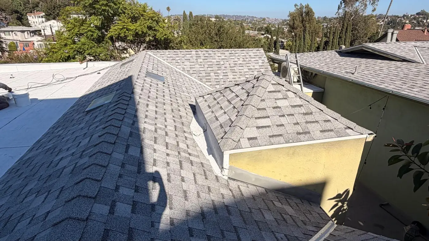 Several hip sections of new gray shingles around a skylight on a Los Angeles apartment roof