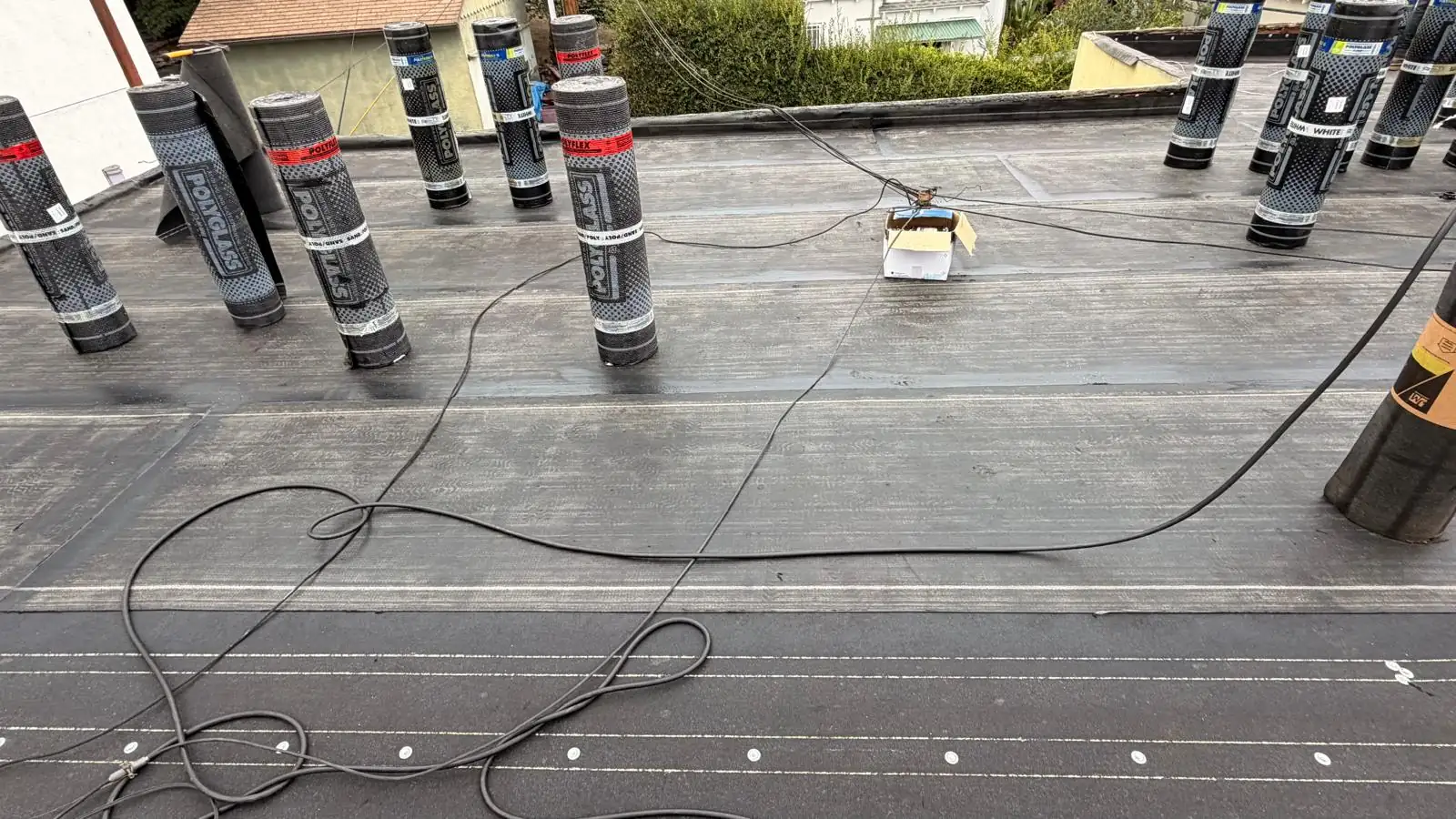 Smooth torch-down first layer on a Los Angeles apartment building flat roof, with white Polyglass cap sheet rolls lined up