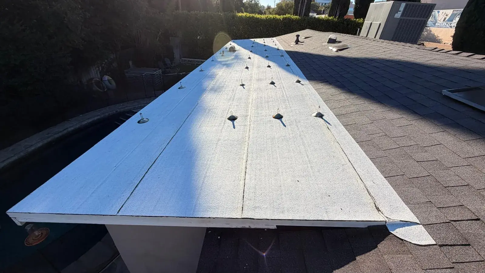 Low roof section in white torch-down roofing beside new dark shingles in Encino