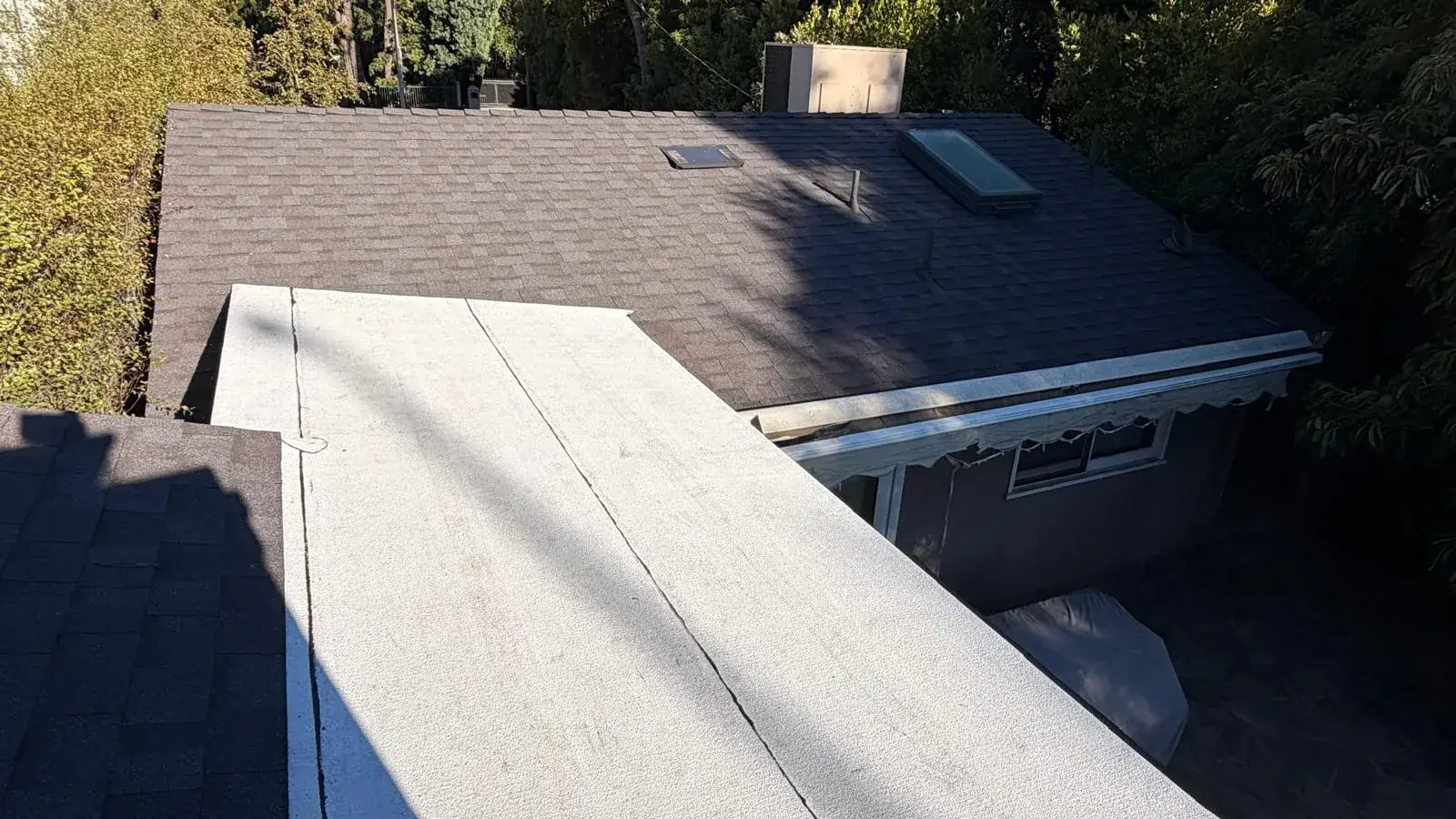 White low-slope roof over a back room next to a dark shingle roof in Encino