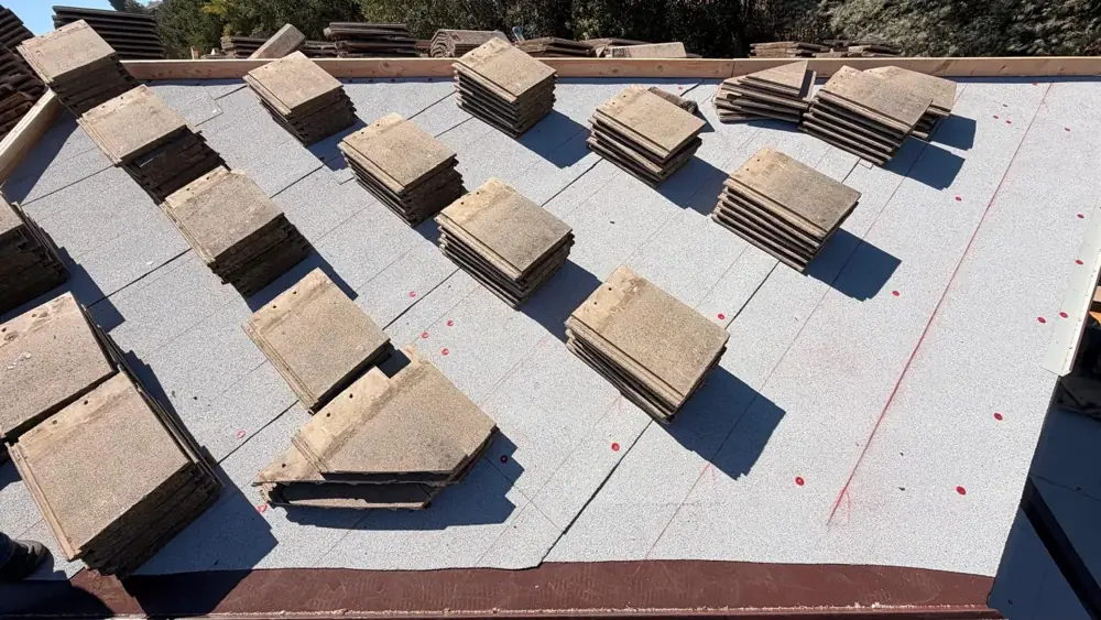 New fire-rated cap sheet underlayment on a tile roof deck with tile stacks staged for relaying