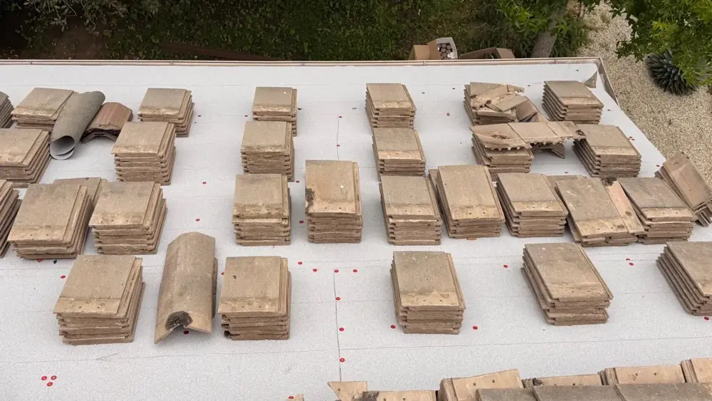 Concrete roof tiles staged on new underlayment, with a few cracked tiles set aside